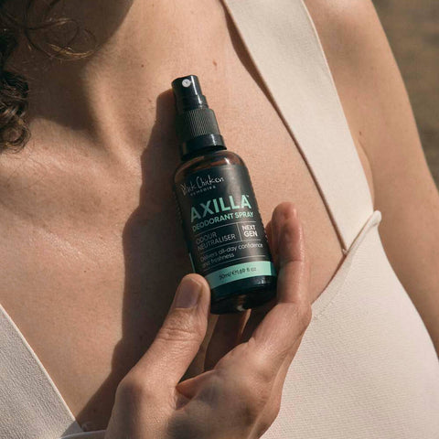 Hand holding 50ml spray bottle of Black Chicken Remedies Axilla Deodorant Spray, combining zinc with all-natural ingredients to neutralise odour, tighten pores, and soothe sensitive skin. Comes in a glass bottle.