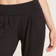 A model wearing black, lightweight lounge pants made of organic bamboo, featuring a draped fit with a wide waistband, tapered leg and two side pockets, showing a closeup of the waist and pockets.