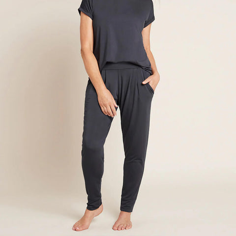 A model wearing navy blue, lightweight lounge pants made of organic bamboo, featuring a draped fit with a wide waistband, tapered leg and two side pockets, showing the front with a hand in pocket.