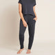 A model wearing navy blue, lightweight lounge pants made of organic bamboo, featuring a draped fit with a wide waistband, tapered leg and two side pockets, showing the front with a hand in pocket.