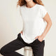 A model wearing a white, lightweight lounge top made of organic bamboo, featuring a softly curved neckline, back seam detail and a subtle curved high-to-low-hem, showing the front.