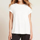 A model wearing a white, lightweight lounge top made of organic bamboo, featuring a softly curved neckline, back seam detail and a subtle curved high-to-low-hem, showing the front.