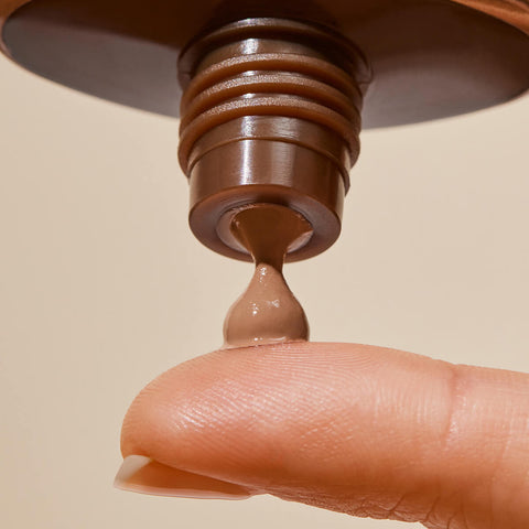 Tube of certified organic natural tinted sunscreen with SPF50+, pink algae and jojoba squeezing product out onto a finger.