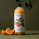 Plastic bottle of mandarin and peppermint natural laundry wash styled with plants and a mandarin on a surface.