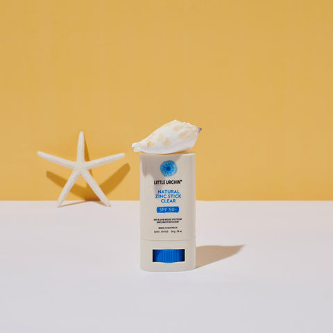 20g tube of Natural Zinc Stick SPF 50+, a clear, hydrating, vegan formula that provides UVA and UVB broad-spectrum protection from the sun while also being 4 hours water-resistant, styled with seashells against a yellow background. Packaged in a cream tube with minimal blue and black text on the label.