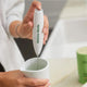 Hand holding Matcha Made Modern Matcha Whisk in a cup, a handheld electric mixer to blend matcha green tea and lattes. Made from stainless steel and comes with a kitchen counter stand.