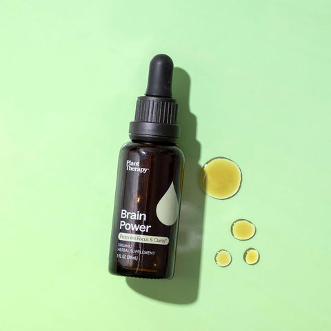 Dropper bottle of an organic herbal supplement for brain health and functionality styled on a surface with drops of the product next to it.