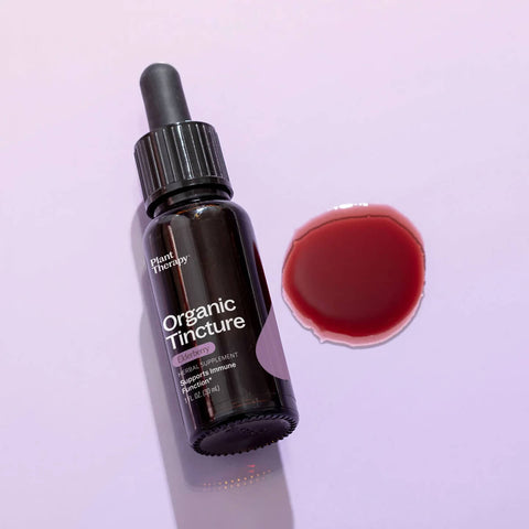 Dropper bottle of elderberry organic herbal supplement styled on a surface with drops of the product next to it.