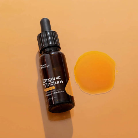 Dropper bottle of turmeric organic herbal supplement styled on a surface with drops of the product next to it.