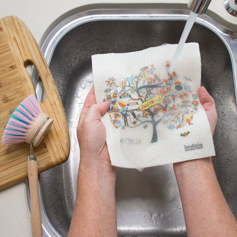 Hands holding a compostable sponge cloth with an Australian design in a sink.