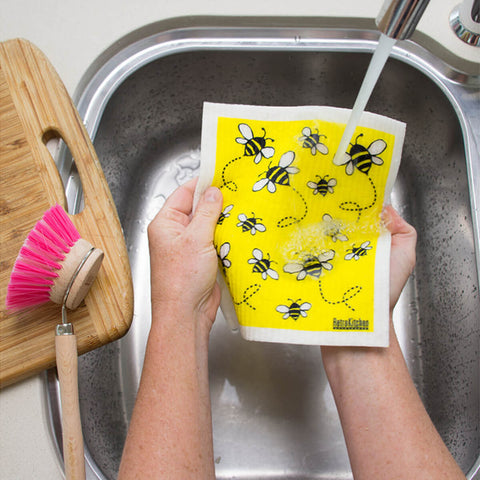 Hands holding a compostable sponge cloth with a bee design in a sink.