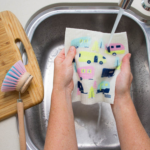 Hands holding a compostable sponge cloth with a caravan design in a sink.