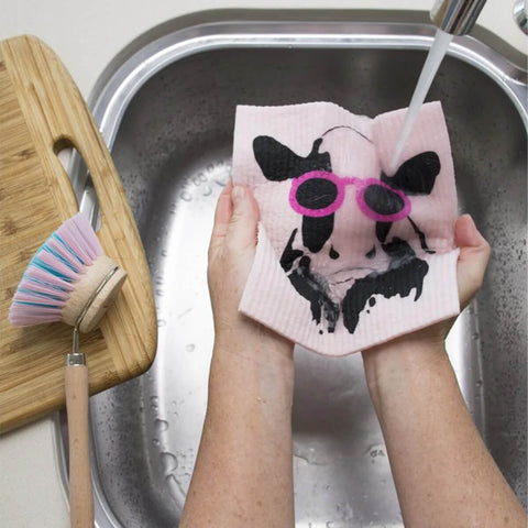 Hands holding a compostable sponge cloth with a cow design in a sink.