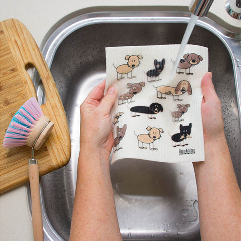 Hands holding a compostable sponge cloth with a dog design in a sink.