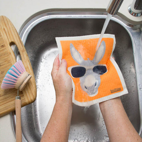 Hands holding a compostable sponge cloth with a donkey design in a sink.