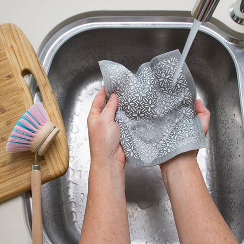 Hands holding a compostable sponge cloth with a geometric design in a sink.