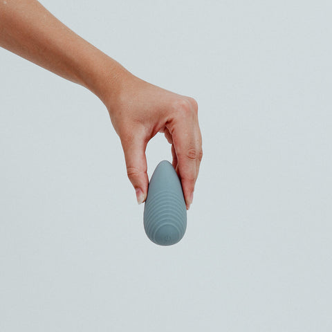 Hand holding Viola Green Eros Palm Vibrator in Stone colour, a small, palm-sized vibrator. Powerful vibrations, effortlessly controlled with a single button. Its grip-friendly design ensures a comfortable and pleasurable experience. Its discreet size also makes it the perfect travel buddy. It's crafted from sustainable materials, such as super silky body-safe silicone and is designed to combine sophistication with eco-consciousness, making it the perfect companion for sustainable pleasure seekers.