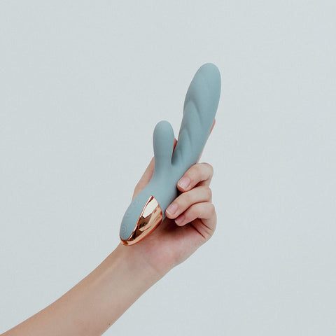 Hand holding Viola Green Essence Rabbit Vibrator in Periwinkle blue colour, a dual-action rabbit vibrator. With whisper-quiet motors and customisable settings, allowing you to tailor all your intimate experiences. Its ribbed shaft adds delightful textures, taking your pleasure to elevated heights. Crafted from sustainable materials, Essence is an eco-friendly choice that combines sophistication with responsible pleasure, ensuring every intimate moment is both satisfying and guilt-free.