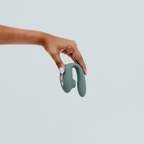 Hand holding Viola Green Maeve Oral Simulator, a dual-headed oral simulation in Seafoam dark green colour. Featuring a combination of vibrating and pulsating sensations. Crafted from sustainable materials and featuring magnetic rechargeable capability, Maeve's removable suction sleeve offers versatile functions for different modes of pleasure. This eco-friendly toy ensures each play session is both satisfying and responsible, truly redefining the art of conscious pleasure.