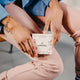 Hands holding a box of 12 waterdrop Microdrink cubes in the Love flavour, featuring pomegranate and goji berry. These sugar-free hydration cubes are made with natural fruit and plant extracts, providing a vitamin-enriched, flavoured drink. Each cube dissolves to create 400-600ml of a refreshing beverage. The product comes in a white box with pink pomegranate and goji berry plant illustrations on the front.