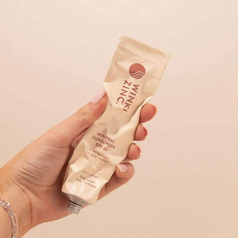 Hand holding 100g aluminium tube of WInki Zinc's Mineral Sunscreen SPF 50, a natural, zinc-based formula that protects against harmful UVA/UVB rays while gently moisturising the skin with vitamin E and coconut oil.